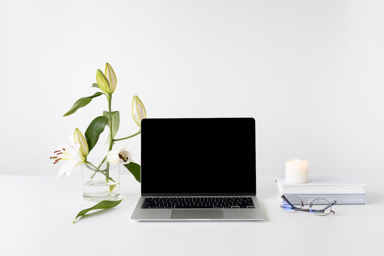 services-03 Elegant minimalist desk setup with laptop, white lilies, books, and candle.